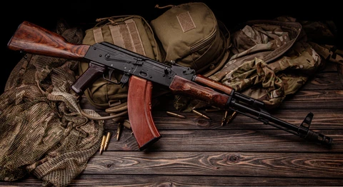 Must-have AK-47 gear including a rifle, military bags, and tactical accessories on a wooden surface