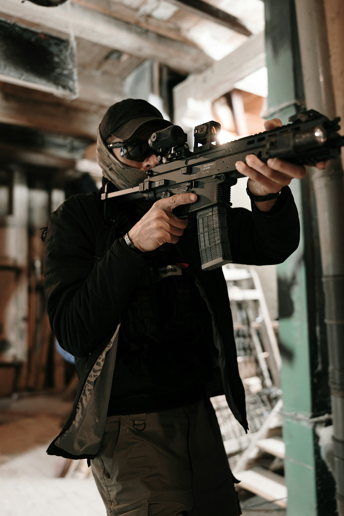 Man aiming a tactical rifle with scope indoors.