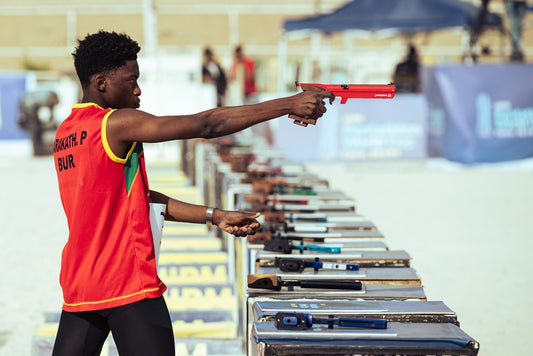 Young athlete practices shooting with a red pistol outdoors.