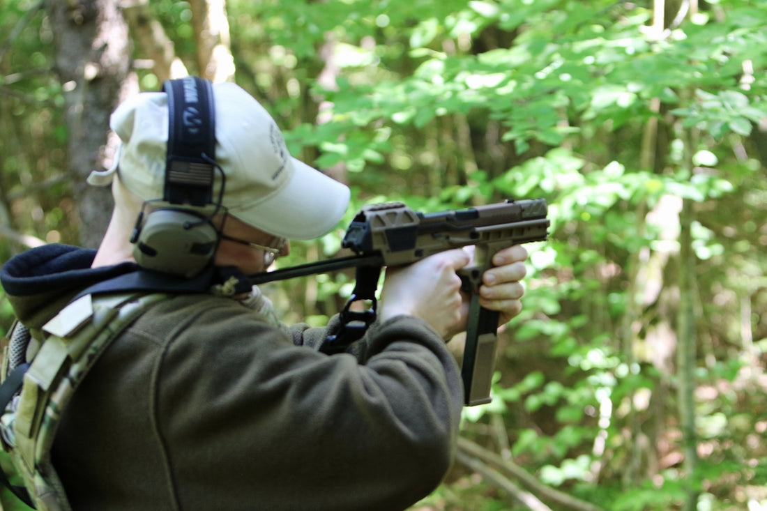 Person aiming a firearm in a forest.
