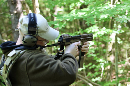 Person aiming a firearm in a forest.