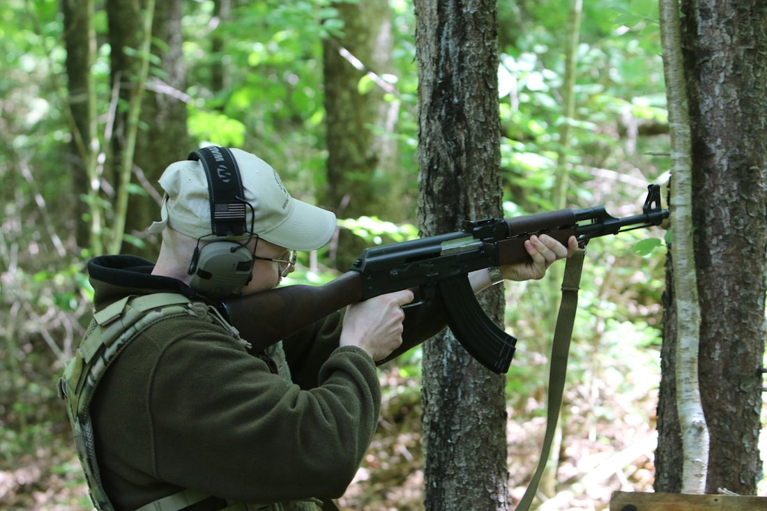 Man in tactical gear shooting rifle in woods.