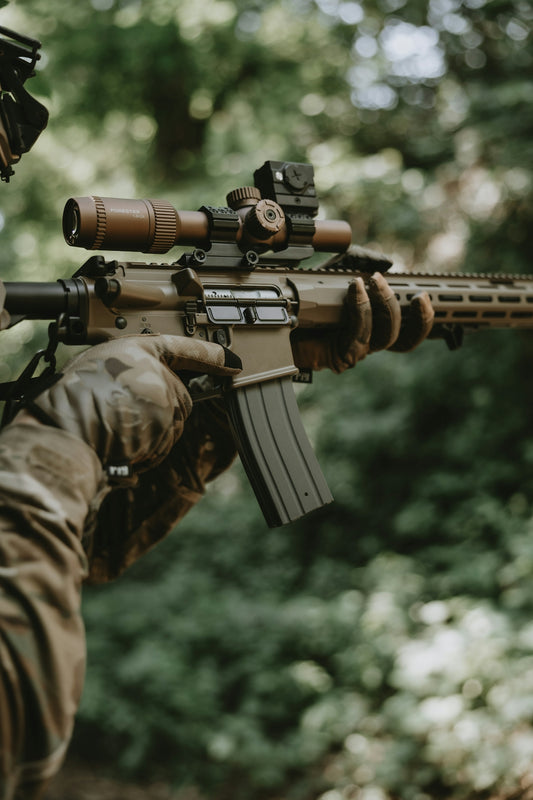 Tactical rifle with scope held by gloved hands in forest.