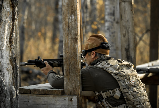Man in tactical gear aiming rifle from wooden cover